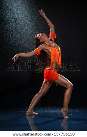 Woman dancing under rain in orange dress. Studio