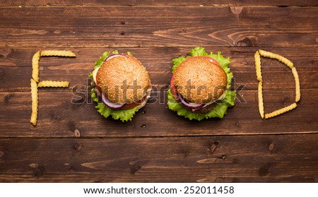 Tasty big burgers with french fries forming word food on wooden background
