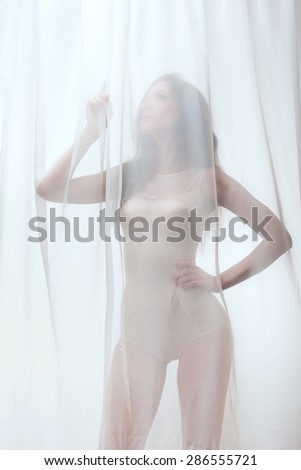 Sexy  lady with perfect fit body in combidress   behind tulle curtain