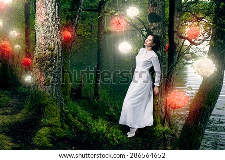 Young beautiful woman in long white  dress walking in the forest with decorative flowers on the trees