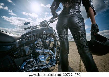 Biker girl in leather jacket standing by a motorcycle. Rear view