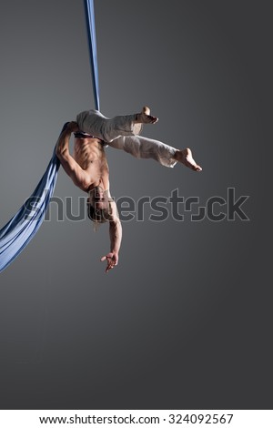 Sporty young man doing exercise with elastics, aerial silk ribbons, aerial. Sport training gym and lifestyle concept. Anti-gravity yoga.
