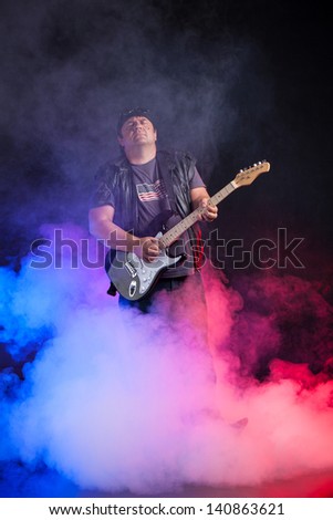 old school rock musician is playing electrical guitar. Shot in a studio.