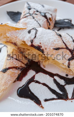 Piece of cherry strudel with chocolate. All sprinkled with powdered sugar.