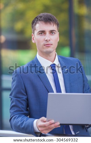 Work in full swing. Successful businessman standing in the street holding a laptop