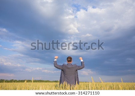 Happy businessman standing on the field to face the sky