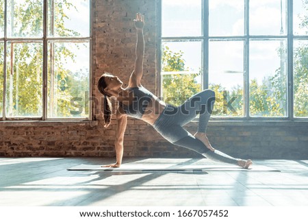 Young sporty fit woman trainer do practice individual hatha yoga instructor training Vasisthasana side plank,arm leg support balancing pose modern gym mat wooden floor window healthy lifestyle concept