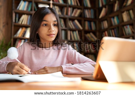 Indian latin girl school pupil distance learning online at remote virtual class with teacher by video conference call, watching webinar, zoom meeting lesson on digital tablet at home, in classroom.