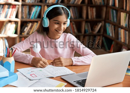 Happy indian latin preteen girl school pupil wearing headphones distance learning online at virtual class with teacher tutor on laptop by video conference call, watching tv lesson at home. 商業照片 © 