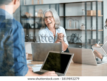 Happy mature old female mentor coach supervisor training young interns at group office meeting professional workshop. Cheerful middle aged teacher professor laughing with students at university class.