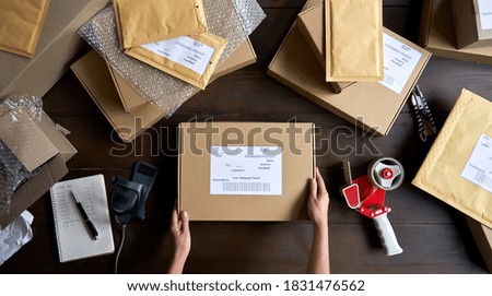Above table top view of female warehouse worker or seller packing ecommerce shipping order box for dispatching, preparing post courier delivery package, dropshipping shipment service concept.