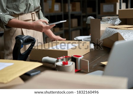 Female small business owner using mobile app on smartphone checking parcel box. Warehouse worker, seller holding phone scanning retail dropshipping package postal parcel bar code on cell technology.