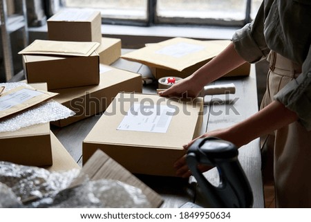 Female distribution warehouse worker or seller packing ecommerce shipping order box for dispatching, preparing post courier delivery package, dropshipping commerce retail shipment service concept.