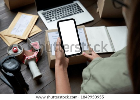 Female warehouse worker, seller, dropshipping small business owner holding phone mock up screen ad scan retail package postal parcel bar code on commercial shipping box on smartphone using mobile app.