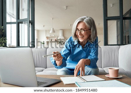 Happy mature older woman video calling on laptop working from home. Smiling 60s middle aged businesswoman talking by conference online virtual chat using computer at home office sitting on couch.