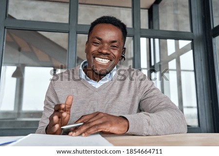 Cheerful african business man talking to web cam on conference call. Happy black businessman, coach, tutor wearing headset laughing, looking camera during webinar, online class, webcam view. Headshot