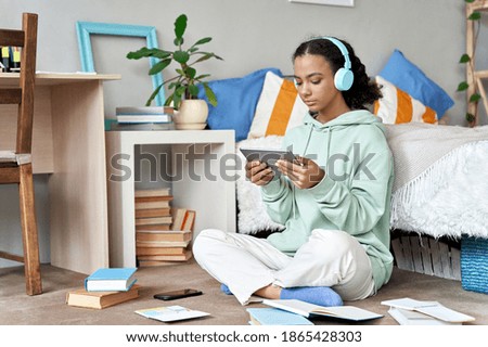Mixed race african teen girl wearing headphones elearning using digital tablet at home, conference calling, watching video class, taking language course in online virtual chat sit in bedroom on floor. Imagine de stoc © 