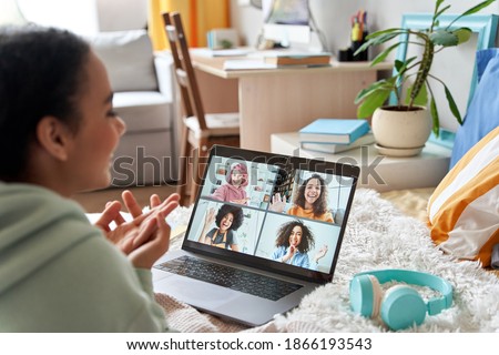 African teen girl talking with friends on distance video group conference call in bedroom. Mixed race teenager having fun chatting during virtual meeting at home communicating online lying in bed.