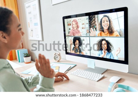 Mixed race teen girl waving talking to happy diverse teenage friends during online virtual chat video call in group conference distance chat virtual meeting using computer at home. Over shoulder view.