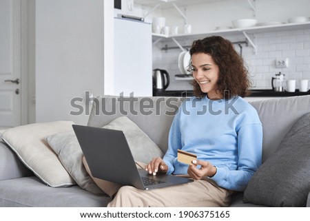 Smiling happy young 20s woman customer, shopper, consumer making online purchase holding credit card using laptop computer at home. Fashion ecommerce shopping and secure internet payments concept.