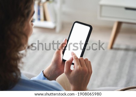 Young woman or teen girl hands holding cell phone touching finger mockup white blank display, empty screen for social media app ad at home. Mobile application tech concept, over shoulder closeup view.