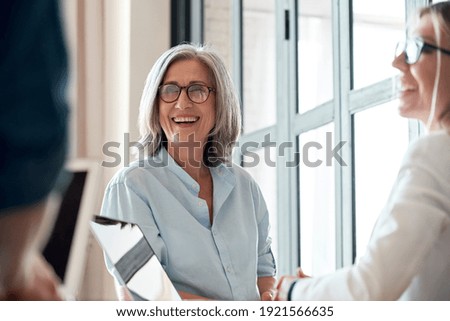 Happy mature old female mentor coach supervisor training young interns at group office meeting professional workshop. Smiling middle aged teacher professor laughing with students at university class