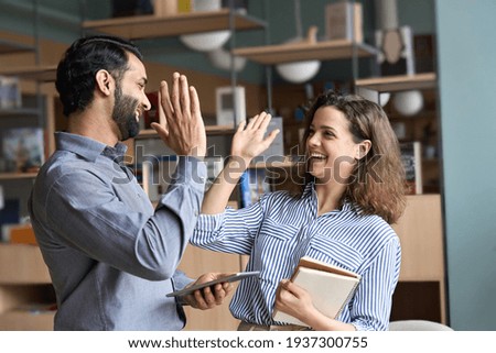 Photo of Two happy friendly diverse professionals, teacher and student giving high five standing in office celebrating success, good cooperation result, partnership teamwork and team motivation in office work.