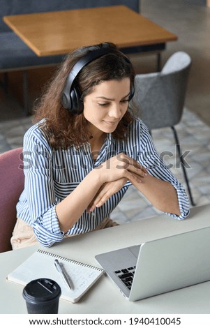 Hispanic girl college student wearing headphones watching distance online learning web class, remote university webinar or having talk on laptop video call virtual meeting seminar at home or campus.