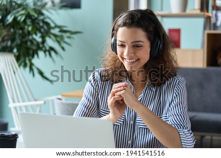 Happy latin hispanic girl college student wearing headphones watching distance online class, remote university webinar or having talk on laptop video conference call virtual meeting at home or campus.