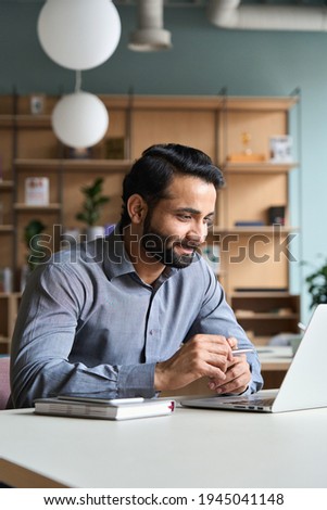 Smiling bearded indian businessman working on laptop at home office. Young indian student using computer remote studying, virtual training on video call meeting, watching online webinar or seminar.