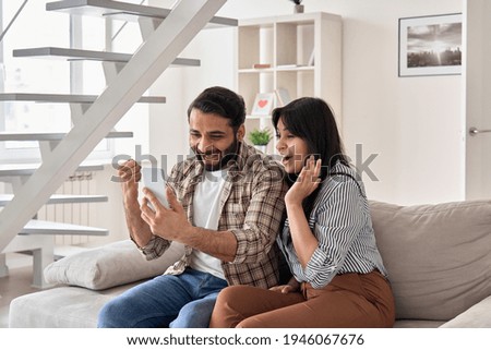 Excited happy young indian family couple winners look at smart phone celebrate win, success, watching game, winning online lottery, reading great news, get shopping discount in mobile message at home.