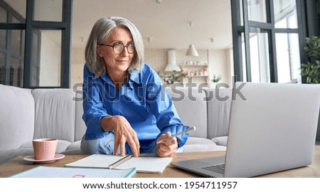 Senior mature older senior adult professional business woman working on laptop from home office, having virtual video call meeting, watching online training webinar e learning class using computer.