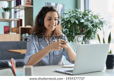 Young adult happy smiling Hispanic indian student wearing headphones talking on online chat meeting using laptop in university campus or at virtual office. College female student learning remotely.
