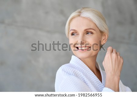 Headshot of happy smiling gorgeous middle aged woman wearing bathrobe at spa salon hotel looking away. Advertising of bodycare spa procedures antiage dry skin care products concept.