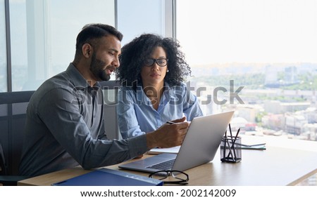 Indian male ceo executive manager mentor giving consultation on financial operations to female African American colleague intern using laptop sitting in modern office near panoramic window. Foto d'archivio © 
