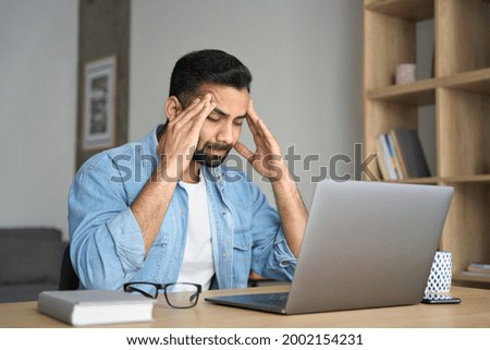 Young indian exhausted business man massaging temples suffering from headache in modern home office with laptop on desk. Overworked burnout academic Hispanic student feeling migraine head strain. Photo stock © 