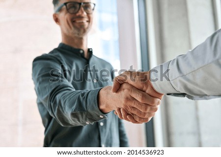 Two happy diverse professional business men executive leaders shaking hands at office meeting. Smiling businessman standing greeting partner with handshake. Leadership, trust, partnership concept.