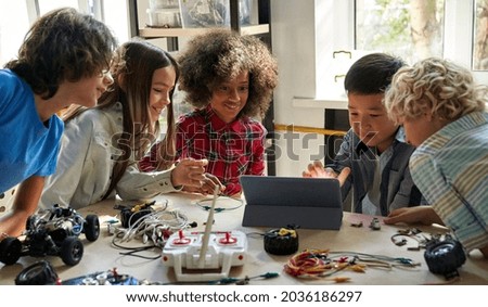 Happy diverse school children students group building robotic vehicle robot cars using tablet computer education software apps. Kids learning programming sit at table at STEM coding engineering class. Stockfoto © 