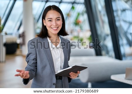 Photo of Happy young Asian saleswoman looking at camera welcoming client. Smiling woman executive manager, secretary offering professional business services holding digital tablet standing in office. Portrait