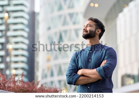Photo of Confident rich eastern indian business man executive standing in modern big city looking and dreaming of future business success, thinking of new goals, business vision and leadership concept.