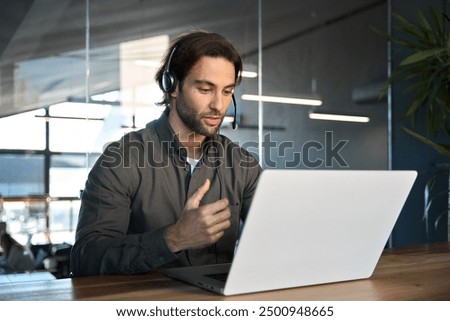 Busy male support service operator talking to customer sitting at desk. Young professional business man call contact center agent wearing headset working in business office using laptop computer.