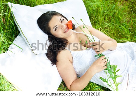 portrait of beautiful young woman laying on a green grass with flower in a park