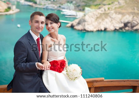 Young couple in love the bride and groom with a bouquet posing on the background beautiful mountains and bays of the wedding day in the summer. Enjoying a moment of happiness and love.
