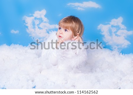 Beautiful baby girl with angel wings in white clothes posing on a background of the sky with clouds - decorated in the style of a little angel in the clouds. A series of photos in my portfolio.
