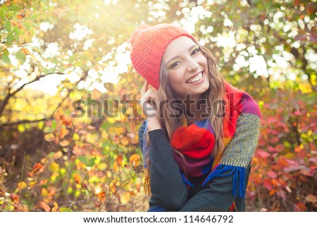 Happy elegant young woman in a knitted red hat posing against colorful fall forest. Early autumn in October.