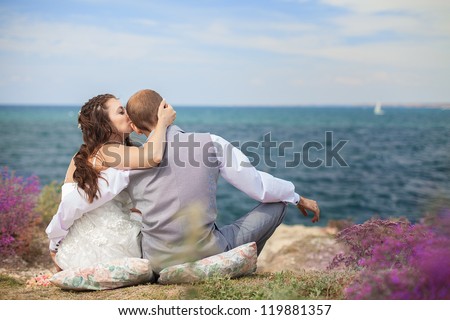 The bride and groom are sitting back watching the sea. Enjoy a moment of happiness and love in their wedding day