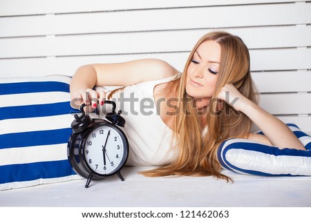 Beautiful young woman lying on the bed. In the foreground is a big clock. Morning awakening