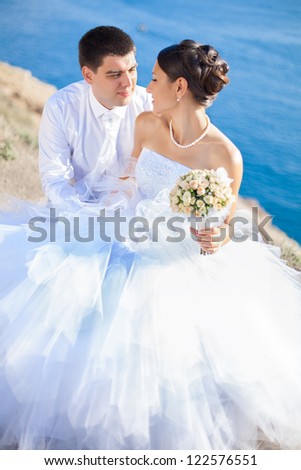 Couple in love young bride and groom dressed in white hugging on cliff background of blue sea in their wedding day in summer