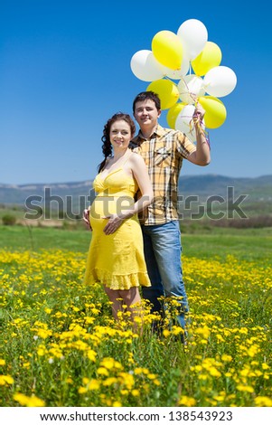 young couple man and his pregnant wife in a field with balloons