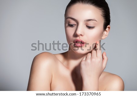 Naturally beautiful brunette woman with flawless skin touching her face over gray background